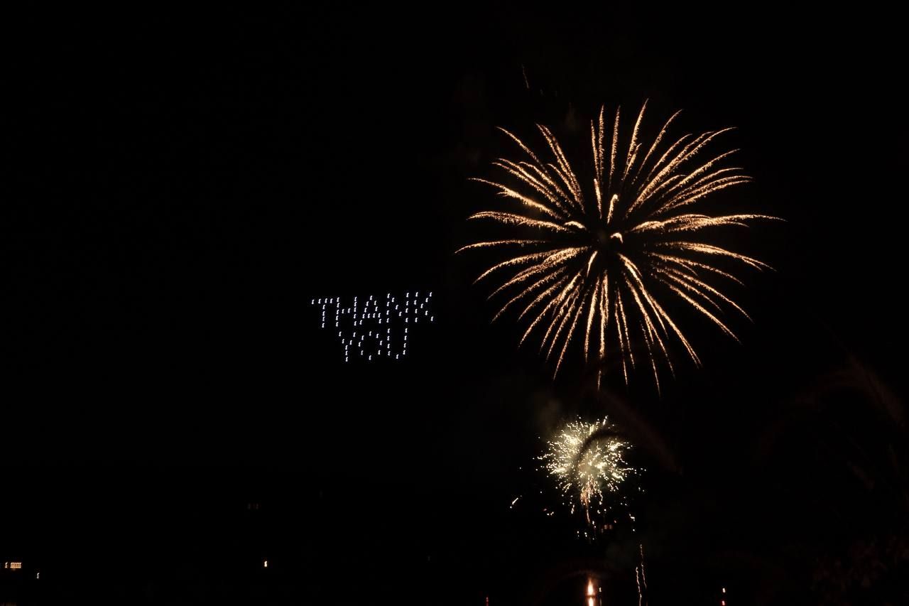Drones spelling THANK YOU in the night sky beside a gold firework burst